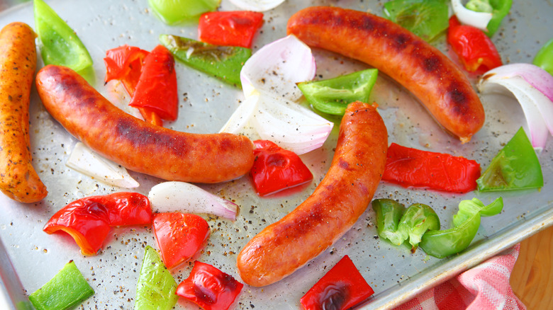 Overhead view of sheet pan meal of sausages, onions and bell peppers with dishcloth