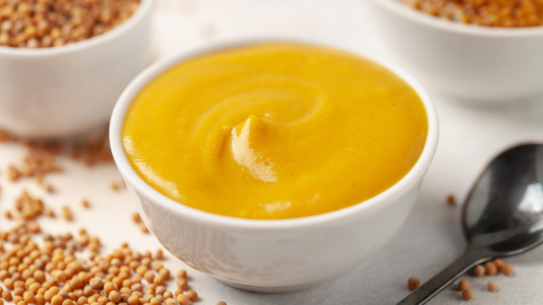 Mustard sauce in a bowl and seeds on a bright background.