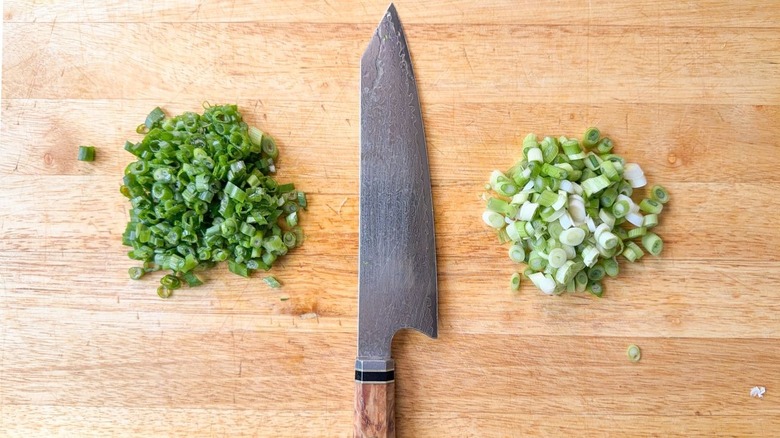 Green and white scallion slices in piles with knife on cutting board