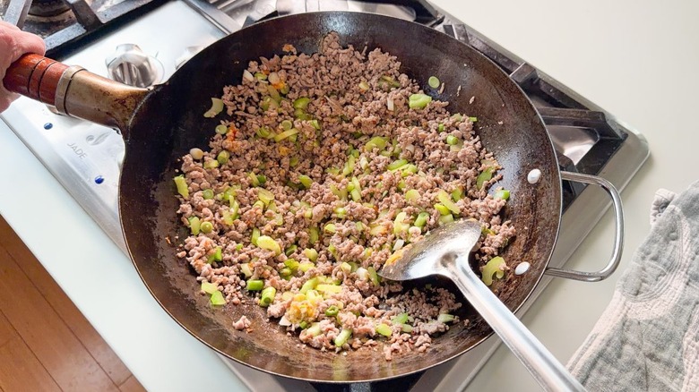 Sautéing ground pork, scallions, celery, garlic, and ginger in wok on stovetop
