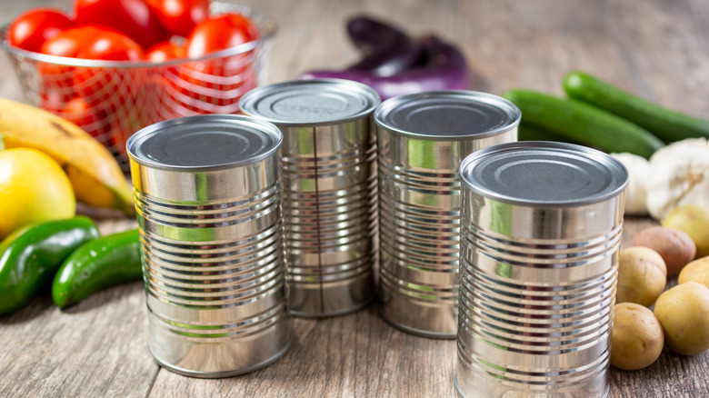 Unmarked tin cans are arranged with other ingredients like tomatoes and peppers.