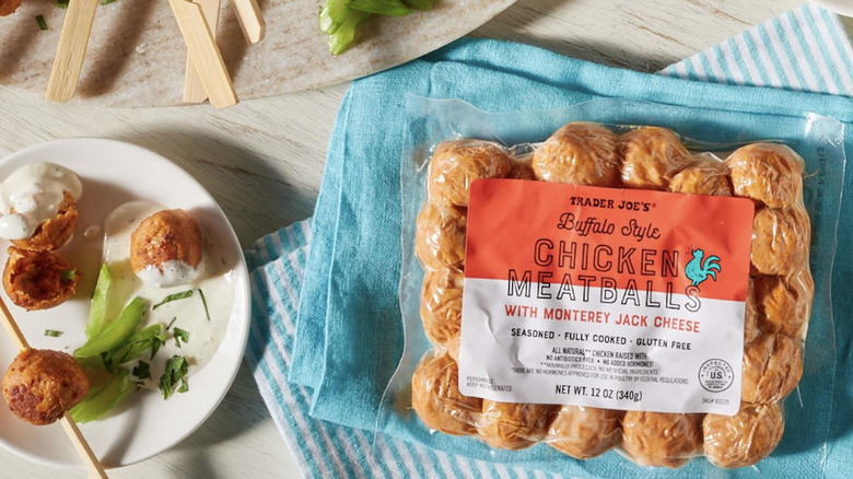 A package of Trader Joe's Buffalo Style Chicken Meatball sits on top a blue cloth, next to a white plate with meatball skewers