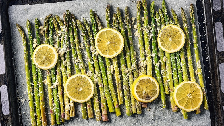 Roasted asparagus with grated parmesan cheese and lemon slices on a parchment-covered sheet pan
