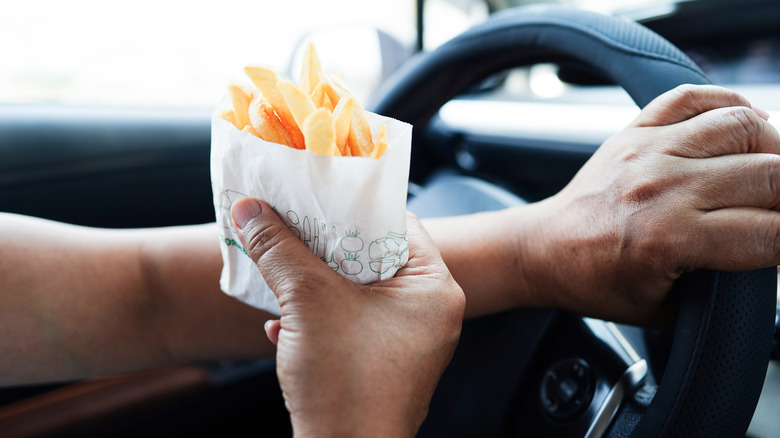 Person driving while holding fast food French fries