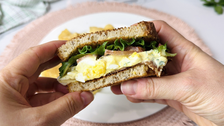 hands holding egg salad club sandwich