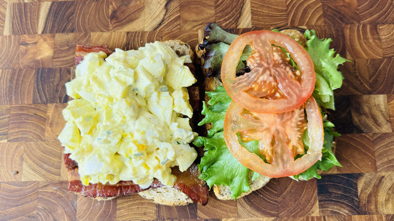 Open faced egg salad club sandwich on wooden board