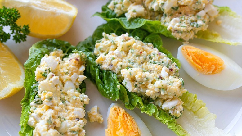 Cottage cheese egg salad on romaine lettuce leaves, cut lemons, and quartered hard-boiled eggs on a white plate.