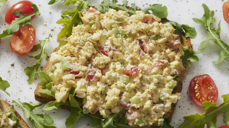 Open faced egg salad and tomato sandwich on white counter.