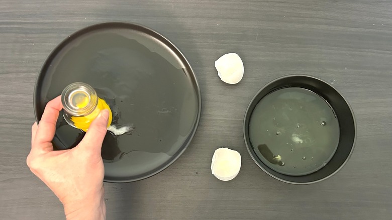 Hand holding a shot glass placed over an egg yolk on a plate alongside a bowl full of egg whites