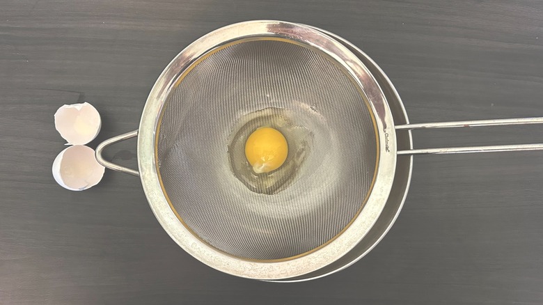 Egg cracked into a fine mesh sieve placed over a metal bowl
