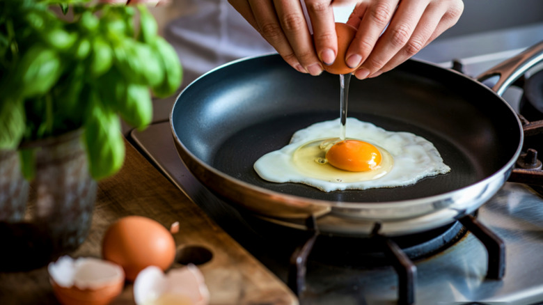 person cracking egg into hot pan