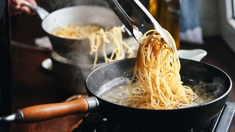 Adding cooked spaghetti to a skillet.