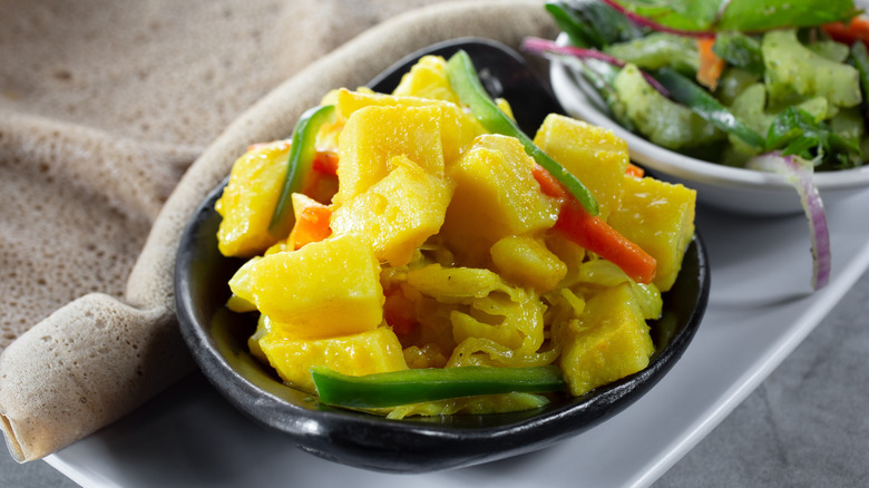 Tikil gomen in a bowl next to injera and salad