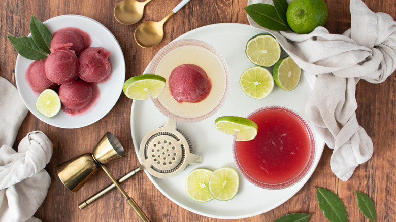 Scoops of sorbet on plate next to sorbet cosmopolitan cocktails and limes