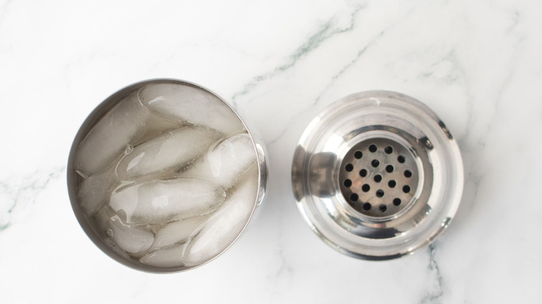 Shaker full of ice and liquids next to lid