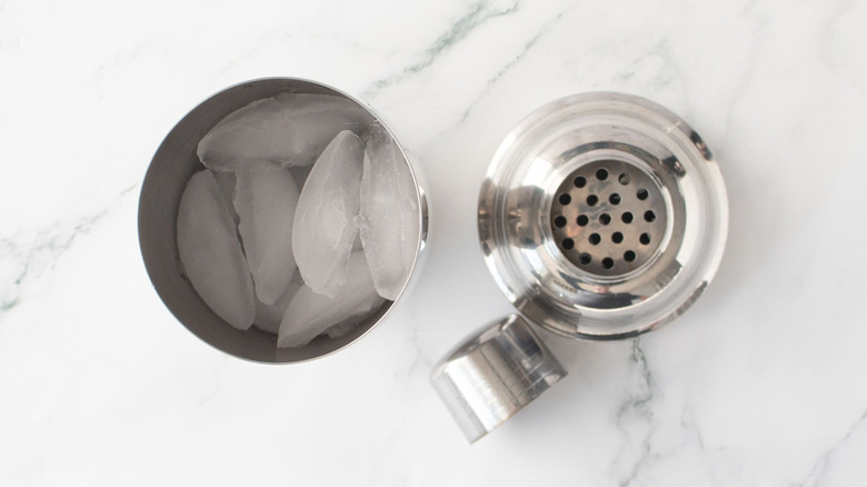 Cocktail shaker full of ice next to lid