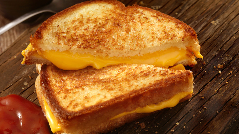 Grilled cheese sandwich cut in half on a wooden board with cheese melting out of the middle