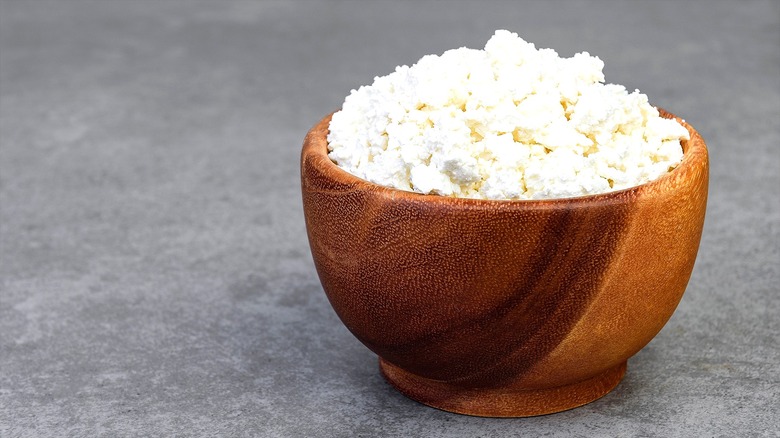 Cottage cheese in a wooden bowl on a gray surface.