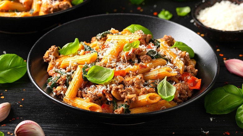 A bowl of penne pasta topped with ground beef and basil leaves.