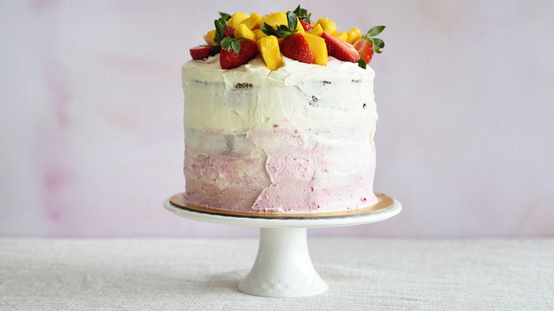 Tall frosted cake toped with mangoes and strawberries