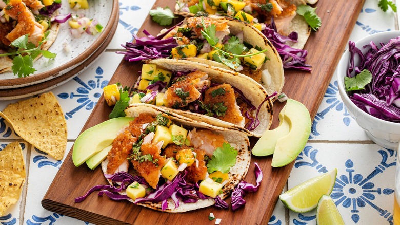 A wooden tray of tacos with avocado