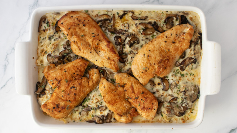 Baked noodle casserole dish topped with seared chicken and fresh herbs