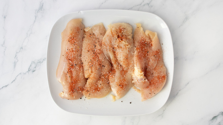 Raw chicken breasts on a plate sprinkled with seasoning