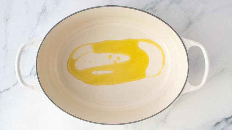 Olive oil drizzled in a large white Dutch oven