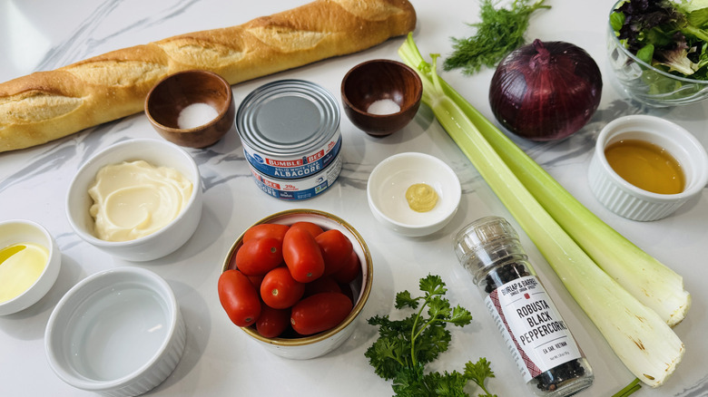 Baguette, bowl of mayonnaise, cans of tuna, and other tuna salad sandwich ingredients laid out