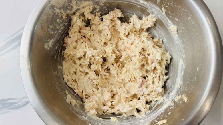 Shredded tuna mixed with mayonnaise and mustard in stainless steel bowl