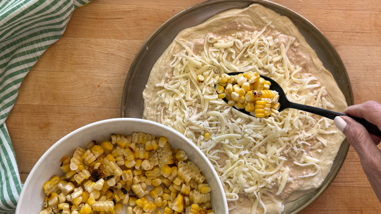 hand adding corn to pizza