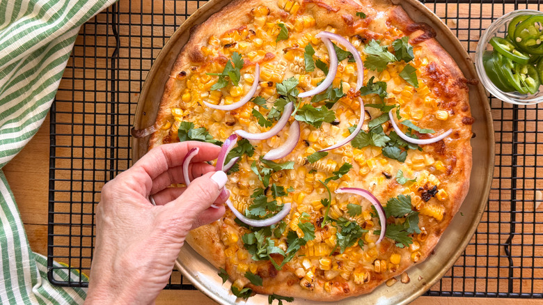 hand adding onions to pizza