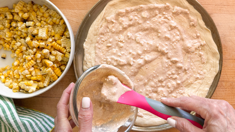 hand adding sauce to dough