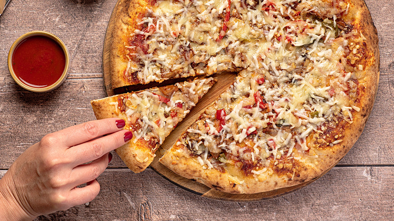 A hand reaches for a slice of a pulled pork pizza.