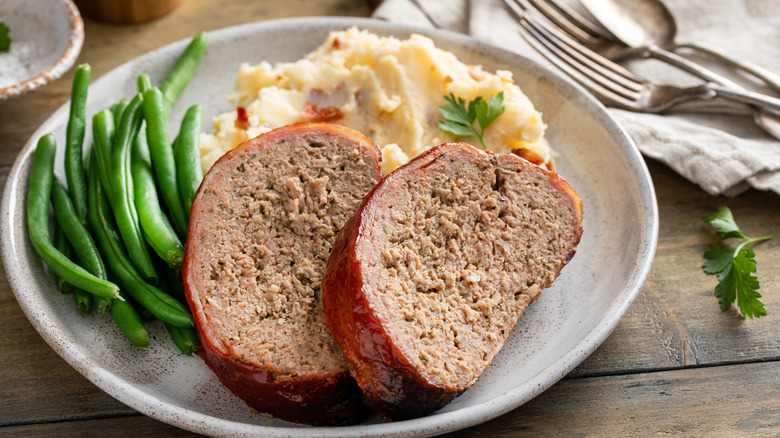 Meatloaf served on a plate with a side of mashed potato and greens