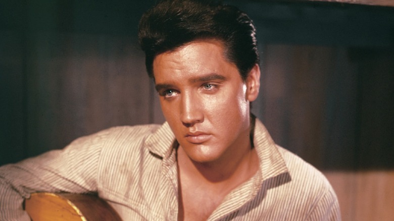 Portrait photo of Elvis Presley playing guitar.