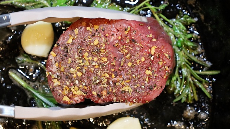 Tongs placing steak fat-side down in skillet