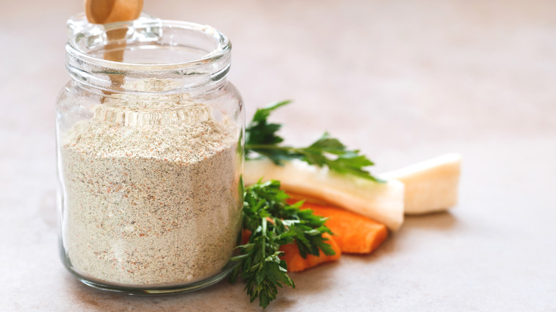 Jar of seasoning with wooden spoon and cut vegetables