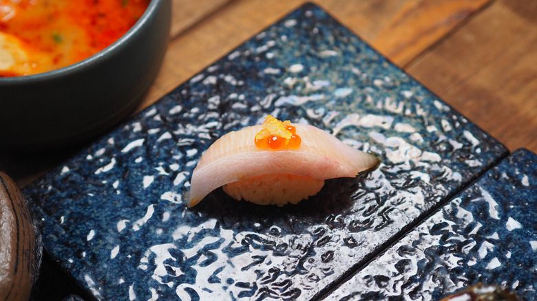 Hamachi sushi on a black plate.