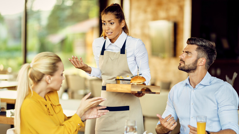 Unhappy seated customers appear to argue with a restaurant server.