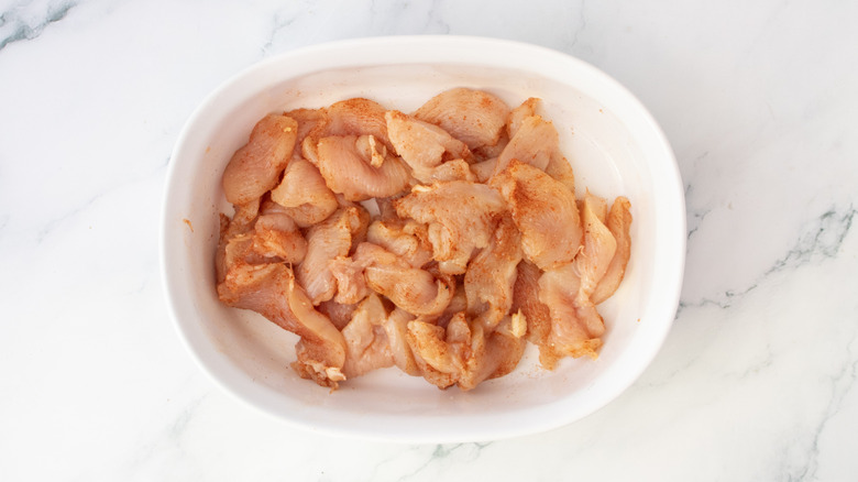 Sliced raw chicken breast in a large bowl coated with seasoning