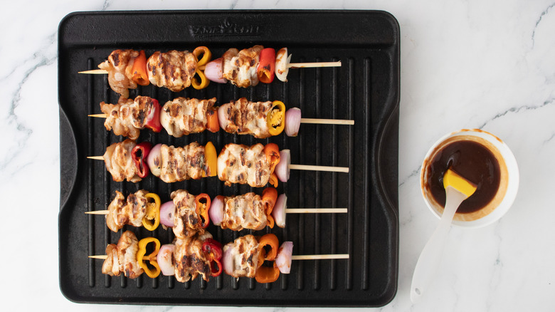 Grilled and skewers on a grill pan with barbecue sauce on the side