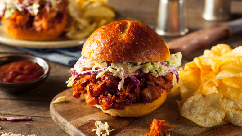 A vegan BBQ pulled pork sandwich with coleslaw and potato chips on a wooden board