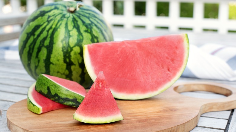 Whole and sliced seedless watermelon on a wooden cutting board