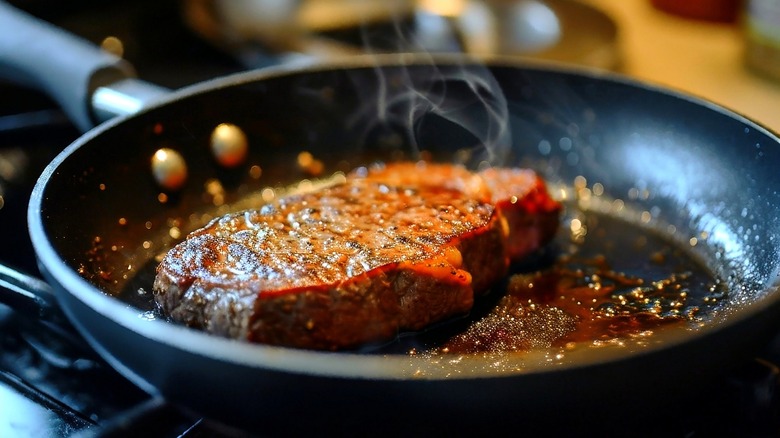 a steak developing a crispy sear on a pan