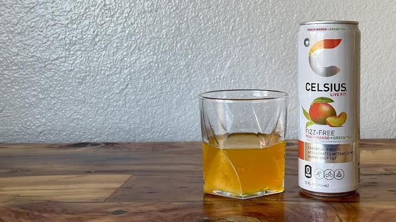 Can and glass of Fizz-Free Peach Mango + Green Tea Celsius on a wooden tabletop