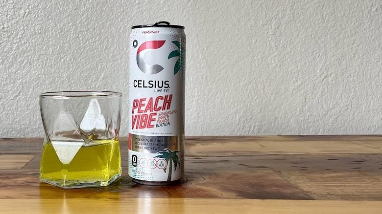 Can and glass of Peach Vibe Sparkling White Peach Celsius on a wooden tabletop
