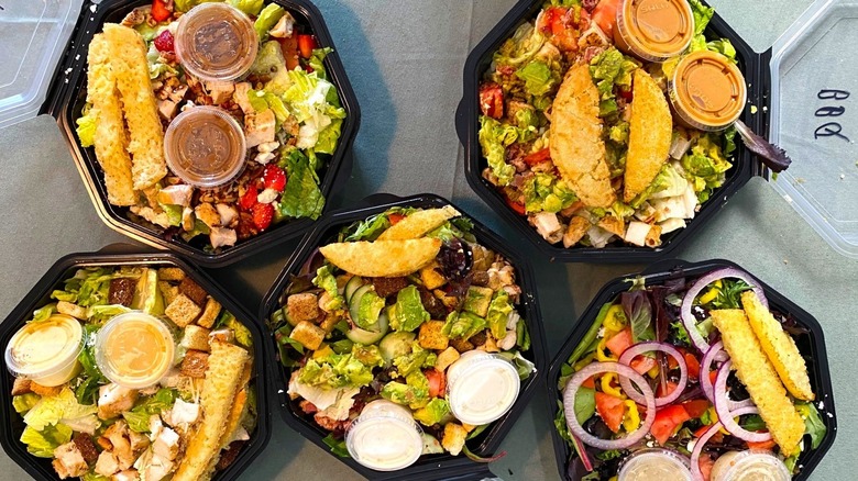 five Schlotzsky's salads open in to-go containers on a table