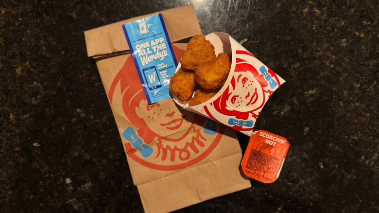 Sleeve of Wendy's Chicken Nuggets and Scorchin' Hot sauce cup resting on to-go baggie