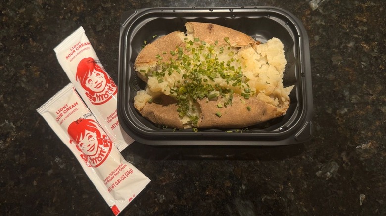 Wendy's Sour Cream and Chive Baked Potato in black to-go container with two packets of sour cream beside it